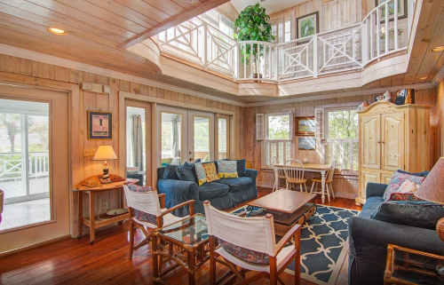 Cozy living room with wooden walls, blue sofas, a coffee table, and large windows letting in natural light.