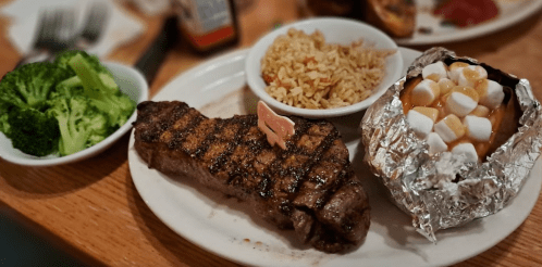 A plate with grilled steak, rice, broccoli, and a baked potato topped with caramel and marshmallows.