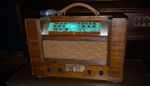 A vintage wooden radio with a glowing dial, featuring a handle and buttons at the front.