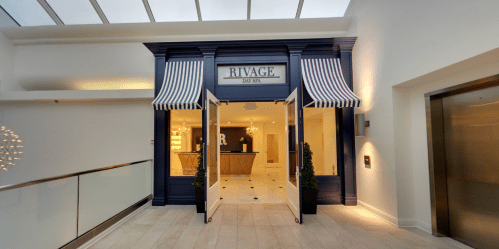 Entrance of Rivage Day Spa, featuring a welcoming reception area and stylish blue decor with striped awnings.