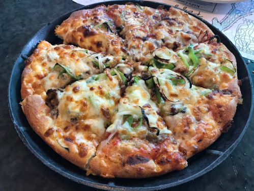 A freshly baked pizza with melted cheese, vegetables, and toppings, served in a round black pan.