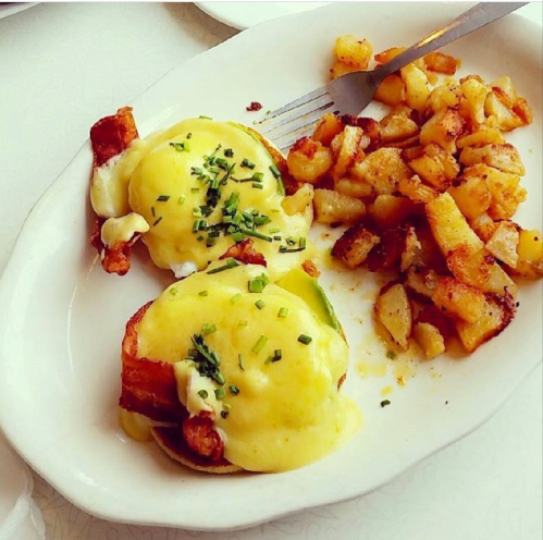 Two eggs Benedict with hollandaise sauce and chives, served with a side of crispy diced potatoes.