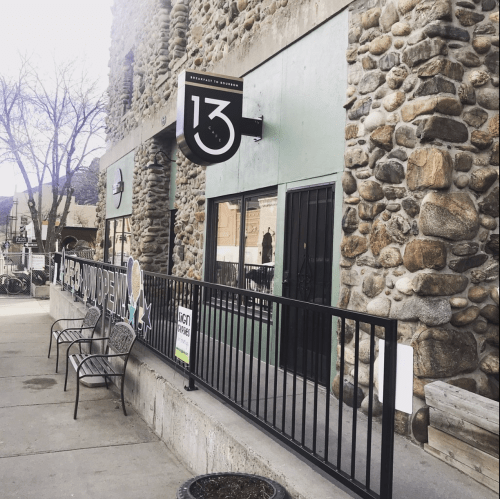 Exterior of a stone building with a sign reading "13" and benches outside, showcasing a welcoming atmosphere.