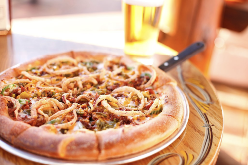 A delicious pizza topped with onions and green peppers, served on a wooden table with a glass of beer in the background.