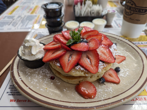 Fluffy pancakes topped with fresh strawberries, whipped cream, and a sprig of mint, served with syrup on the side.