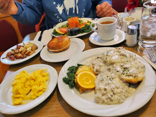 A breakfast spread featuring biscuits and gravy, scrambled eggs, potatoes, a salad, and coffee on a table.