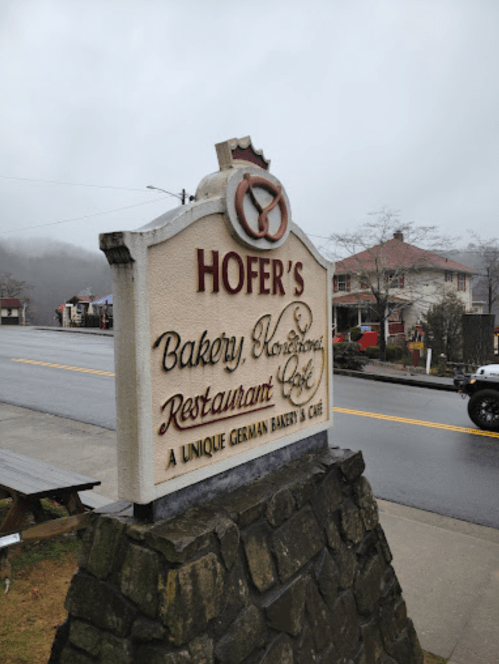 Sign for Hofer's Bakery, Restaurant, and Café, featuring a unique German bakery, set against a foggy backdrop.