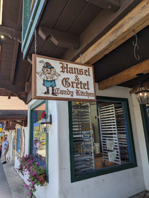 Sign for "Hansel & Gretel Candy Kitchen" hanging outside a charming shop with a rustic wooden facade.