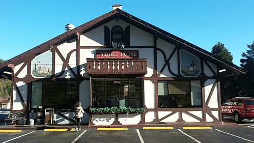 A charming restaurant with a wooden exterior and decorative murals, featuring an "Open" sign and a customer outside.