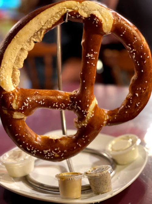 A large, soft pretzel on a stand, served with three dipping sauces on a plate.