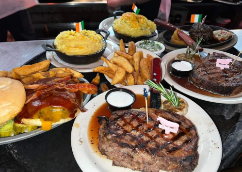 A variety of hearty dishes including steak, mashed potatoes, bacon, fries, and a burger, all served on a platter.