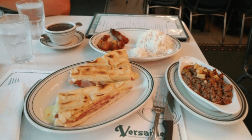 A table setting with a Cuban sandwich, rice, beans, fried plantains, and a small dish of ground meat.