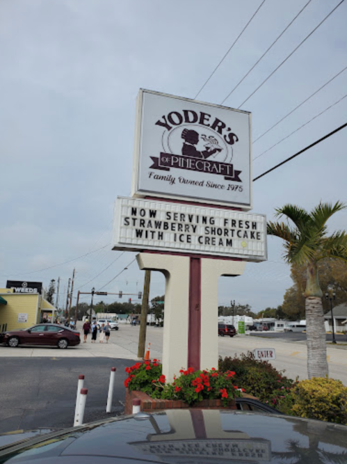 Sign for Yoder's of Pinecraft announces fresh strawberry shortcake with ice cream, surrounded by palm trees and a cloudy sky.