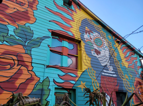 Colorful mural on a building featuring a skull with flowers and vibrant patterns against a blue background.