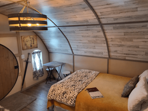 Cozy interior of a small room featuring a bed, table, and unique curved ceiling design. Warm colors and rustic decor.