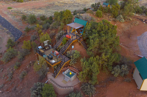 Aerial view of a modern cabin on a hillside, surrounded by trees and featuring a deck and outdoor seating area.