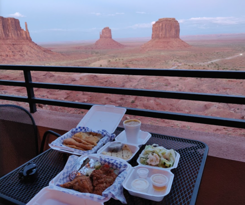 A table with takeout food overlooking a scenic view of red rock formations and desert landscape.