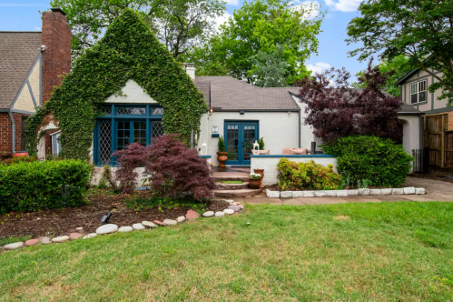 Charming house with ivy-covered walls, blue windows, and a landscaped garden under a clear sky.