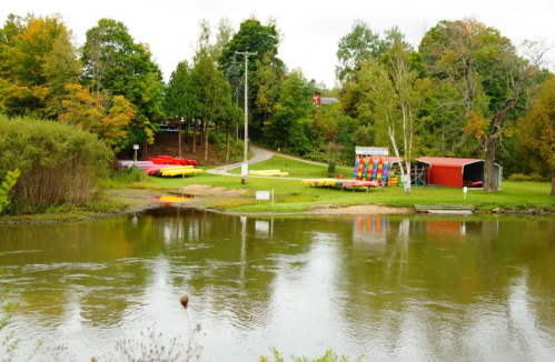 A serene river scene with colorful kayaks, lush greenery, and a path leading to a recreational area.