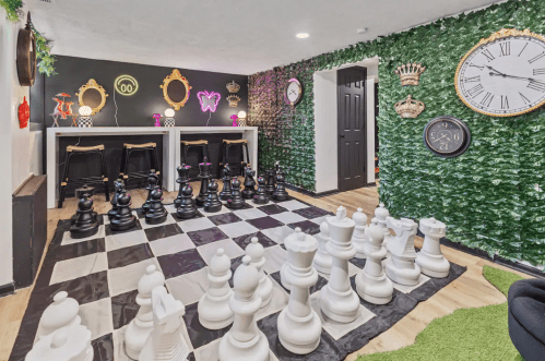 A stylish game room featuring a large chessboard with oversized black and white pieces, surrounded by decorative walls.