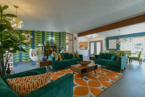 Bright living space featuring teal sofas, a patterned rug, and a vibrant green wall with plants, creating a cozy atmosphere.
