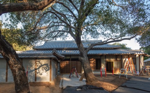 A traditional-style house under construction, surrounded by trees and scaffolding, with a clear blue sky above.