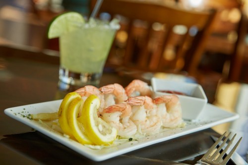 A plate of shrimp with lemon slices and cocktail sauce, accompanied by a glass of lime drink.