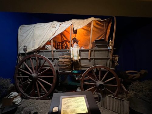 A vintage wagon with a covered top, illuminated from within, displayed against a blue background. A sign is in front.