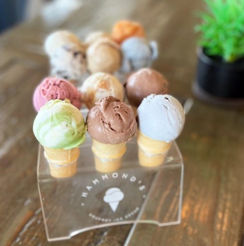 A display of colorful ice cream scoops in cones, arranged in a clear holder on a wooden table.