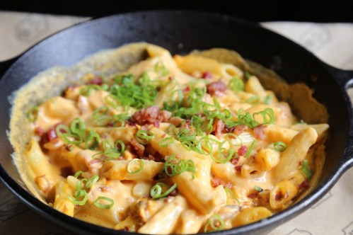 Creamy macaroni and cheese with bacon bits and green onions served in a cast iron skillet.