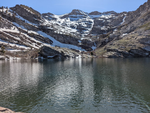 A serene mountain lake reflecting snow-capped peaks and clear blue skies, surrounded by rocky terrain.