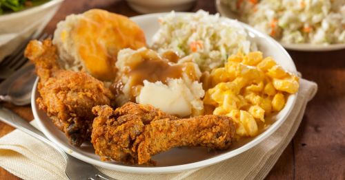 Closeup of a plate of fried chicken drumsticks, mac and cheese, mashed potatoes, coleslaw, and biscuits
