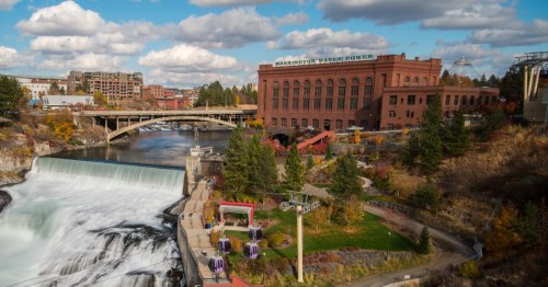 A scenic view of a waterfall with a historic building, bridge, and gondola in a vibrant, urban landscape.