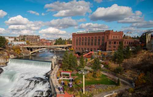 A scenic view of a waterfall and historic building in Spokane, Washington, with clouds and trees in the background.