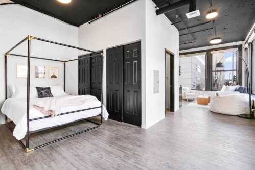 A modern bedroom with a four-poster bed, black doors, and a cozy seating area with large windows.