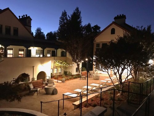 A serene courtyard at dusk, featuring benches, trees, and softly lit pathways between buildings.