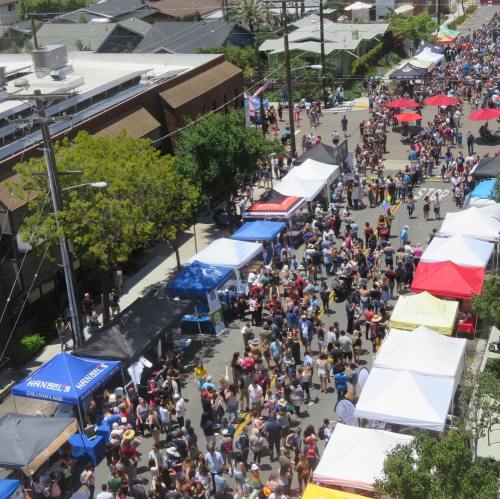 Aerial view of a bustling street fair with colorful tents and a large crowd enjoying the festivities.