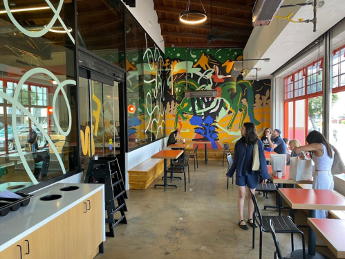 A modern restaurant interior with colorful mural, tables, and patrons enjoying their meals.