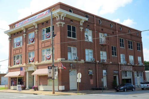 Historic brick building with decorative elements, featuring windows, air conditioning units, and patriotic banners.