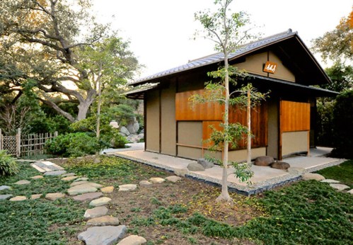 A serene garden scene featuring a traditional Japanese-style house surrounded by greenery and stone pathways.