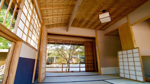 Interior of a traditional Japanese room with sliding doors, tatami mats, and a view of a garden outside.