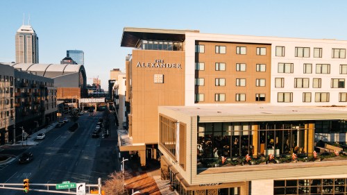 Aerial view of The Alexander hotel in Indianapolis, with city skyline and street visible in the background.