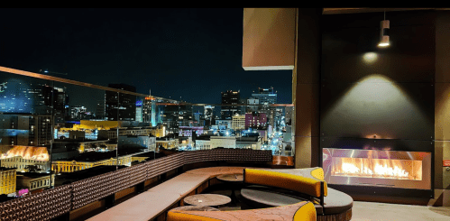 Rooftop lounge with a cozy fireplace, overlooking a vibrant city skyline at night.