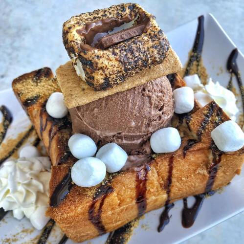 A decadent dessert featuring toasted bread topped with chocolate ice cream, marshmallows, and a s'mores-inspired garnish.