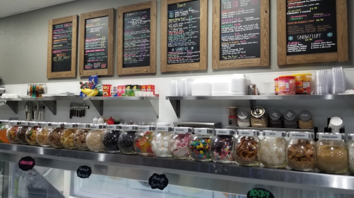 A colorful ice cream shop display with jars of toppings and a menu board above.