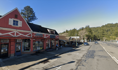 A colorful storefront along a tree-lined street, with shops and a clear blue sky in the background.