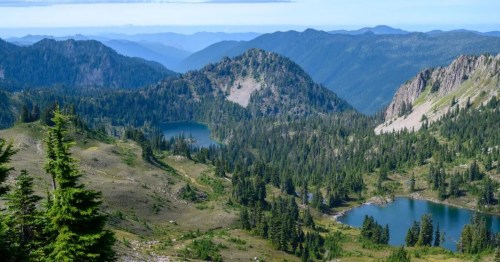 A scenic view of mountains and lakes surrounded by lush greenery under a clear blue sky.