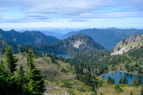 A panoramic view of lush green mountains and serene lakes under a blue sky with scattered clouds.