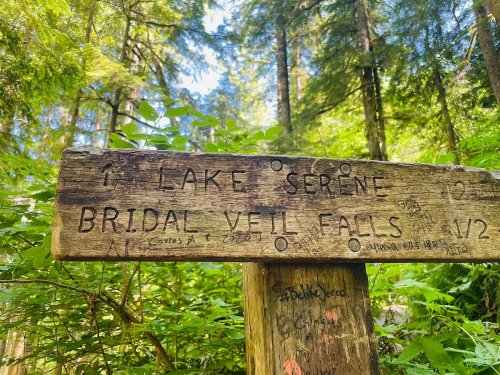 Wooden signpost indicating directions to Lake Serene and Bridal Veil Falls, surrounded by lush greenery.