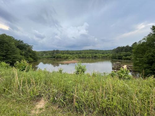 A serene lake surrounded by lush greenery under a cloudy sky, with a small dock visible in the distance.